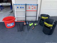 Full overview of the lawn games set: 2 Kan Jam bins, ladder ball ladders with bolas, badminton rackets, baseball bat, football, and red bin