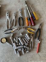 Photo showing a variety of pliers, screwdrivers, ratchets, and numerous chrome sockets spread out on a surface.