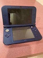 Open Nintendo 3DS XL showing front screens and controls, blue interior color.