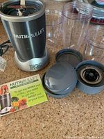 NutriBullet Magic Bullet base with multiple clear blending cups, blade attachments, lids, and instruction pamphlet arranged on countertop.