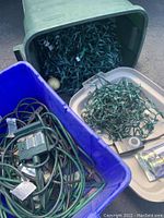 Outdoor string lights coiled inside bins and a green container with other lighting accessories.