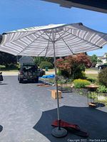 Full view of large outdoor umbrella opened, showing striped canopy and metal pole with weighted base on pavement outdoors