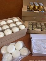Box of 12 round white candles with some loose candles in a plastic bag, next to boxes of gold speckled votive holders and bubble wands.