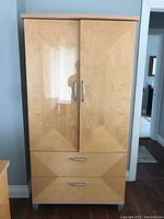 Front view of the beige wood armoire with silver handles, showing two doors and two drawers.