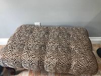 Top view showing brown and white zebra-like animal print fabric upholstery with tufted quilting on bench top.