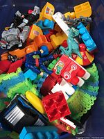 Photo showing the contents of the toy bin, including LEGO Duplo blocks, green and blue toy tracks, green dragon figurine, and several action figures in black, grey, and red.