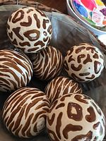 Photo showing six ceramic decorative balls with alternating brown spot and stripe patterns inside a basket.