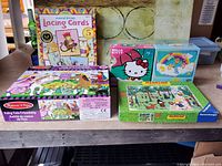 View of five children's puzzles and lacing cards including Melissa & Doug Fairy Tale Friendship, Ravensburger Madeline, Hello Kitty puzzle, rainbow theme puzzle, and eeBoo musical lacing cards.