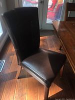 Faux leather dining chair with tufted vertical seams and wooden legs in brown finish next to table.