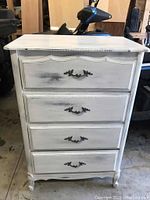 Front view of white washed vintage dresser with four drawers and ornate metal handles.