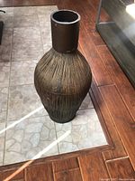 Front view of large brown floor vase on tiled floor, showing full shape and texture.