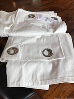 Folded light ivory drapes showing silver metal grommets on light fabric.