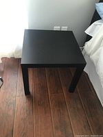 Black square table top showing slight scratches on surface with four legs and wood floor background.
