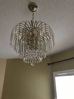 Light fixture off, showing gold metal frame with cascading faux crystal beads hanging down from multiple curved arms, suspended by chain from ceiling.