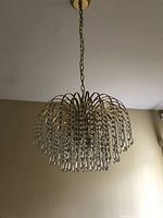 Close-up photo showing gold-tone metal frame with multiple arched arms decorated with hanging vertical strands of clear faux crystals.