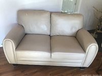 Light beige two-seater sofa with cushioned backrests, corner damage visible on front side corner