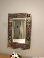 Front view of rectangular mirror with decorative wood frame and colorful tile inlays reflecting part of the room.