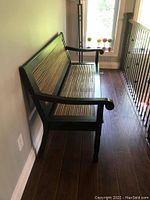 Side view of the brown wooden framed bench with bamboo slatted seat and backrest placed against a light-colored wall