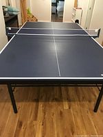 Full view of the foldable ping pong table set up indoors on wood flooring with net attached.