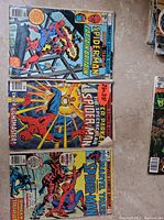 Photo showing three vintage Spider-Man comic books laid out side by side, featuring 'Spider-Man and Captain Britain,' 'Spectacular Spider-Man,' and 'Marvel Tales Spider-Man.'