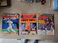 Top-down view of three vintage sports magazines placed on the floor showing front covers featuring baseball and football players.