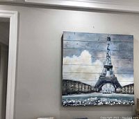 Full view of the wooden wall art painting of the Eiffel Tower hanging on a light colored wall.