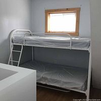 White metal bunk bed assembled in a room with a window, includes upper bunk with guard rail, lower bunk, and angled ladder.