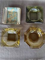 Top view of four ashtrays: three glass in amber and green shades and one painted ceramic with floral design