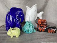 Front view of five ceramic animal-shaped planters and vases placed on a cloth surface against a plain backdrop.