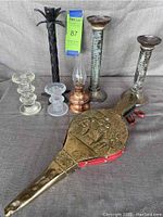 Overview of assorted candlesticks and brass leather bellows showing different materials including glass, metal, copper, and brass with embossed design.