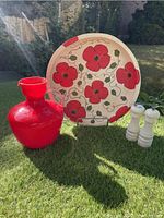 Photo showing full set: round hand-painted wood platter with red poppies, red glass pitcher, wooden salt and pepper grinders on green surface