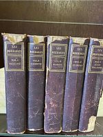 Front spines of the 5 volumes showing title and volume names: Fantine, Cosette, Marius, St. Denis, Jean Valjean. Wear visible on edges and spine tops.