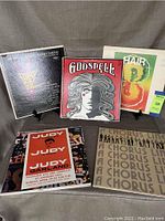 Photo showing 6 LP record covers for musicals Charlie Chaplin, Godspell, Hair, Judy Garland, and A Chorus Line along with printed material