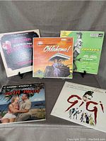 Photo of five vintage LP records from musicals Oklahoma!, Damn Yankees, South Pacific, Gigi, and Rodgers and Hammerstein, displayed standing upright with illustrated covers.