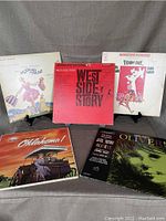 Five LP vinyl records from musicals: The Sound of Music, West Side Story, Funny Girl, Oklahoma, and Oliver with original jackets visible, displayed standing and flat.