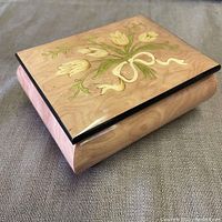 Closed music box showing floral inlay top design with cream-colored tulips and ribbon on light wood.