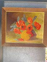 Frontal image of the framed oil painting showing vibrant red poppies and blue flowers in a yellow vase on canvas board with lightweight wooden frame.