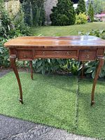 Full view of wooden Queen Anne style writing desk with curved legs and three drawers.