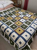 Full view of the crocheted granny square afghan blanket laid out on a mattress, showing multiple squares with multicolor design including green, cream, yellow, blue, and red accents with flower centers.