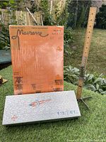 Macrame work board, hem ruler, and Fasturn T-6 tool arranged on grass.