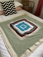Full view of a small square crochet blanket laid flat on a bed showing the entire pattern and shape.