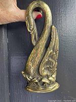 Brass swan door knocker held against a black surface showcasing detailed swan head, feathers and base.