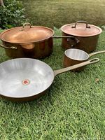 6-piece vintage copper cookware set showing lids, pots, pans with brass handles on grass.