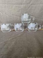 Four clear glass mugs with etched globe maps stacked and arranged on fabric.