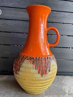 Full side view of the tall orange and yellow textured ceramic vase with handle showing shape and color pattern.