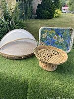 Three vintage trays and basket on grass showing a large round wicker vinyl tray with mesh sides, rectangular bamboo mesh tray with floral liner, and round rattan pedestal basket.
