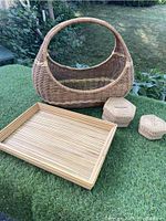 Overview photo of all four items placed on grass — one large handled wicker gondola basket, two small woven nesting baskets with lids, and a rectangular tray.
