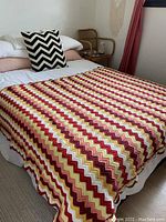 Full view of the zig zag crocheted blanket laid out on a double mattress showing size, color pattern and drape.