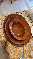 Stacked set of three brown serving bowls on granite counter, showing leaf vine embossed detail on rims