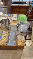 Wide view of all items on granite countertop showing serving trays, vase, plastic and wooden trays, bucket and grater.